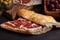 Jamon Iberico with white bread, olives on toothpicks and fruit on a dark background