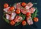 Jamon Serrano sliced with small cherry tomatoes and fresh thyme on black stone background.