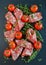 Jamon Serrano sliced with small cherry tomatoes and fresh thyme on black stone background. Top view