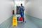 Janitor Holding Mop With Bucket And Wet Floor Sign