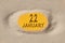 January 22. 22th day of the month, calendar date. Hole in sand. Yellow background is visible through hole