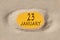 January 23. 23th day of the month, calendar date. Hole in sand. Yellow background is visible through hole