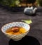 Japanese bowl filled with brown tea, in the background a deliberately blurred teapot