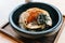 Japanese Chashu Don: Steam Rice topping with Roasted Pork Belly, Yolk, Dried Seaweed and Saffron. Served in black ceramic bowl.