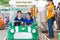 Japanese female Tokyo Dome Amusement Park staff waves at two Asian girls riding on a Furi Furi GP car at Tokyo Dome City