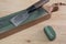 Japanese leather craft knife on a leather knife strop with green polishing compound on a wooden surface