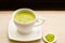 Japanese matcha green tea is poured into a white mug and on a white saucer in powder. Tea set on a textured napkin. Invigorating d