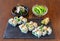 Japanese sushi food with avocado, rice, sea delicacies on a black stone, on a brown background. Plates with salad and
