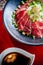 Japanese Tataki raw beef cuisine with ginger, onion, spring onion and soy sauce set on red wooden tray