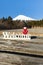 Japanese traditional kokeshi doll dressed in red kimono on top of the word Welcome. Background with Mount Fuji