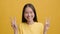 Japanese Woman Gesturing V-Sign With Both Hands Over Yellow Background