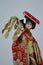 Japanese woman porcelain doll in red coat with decorative red hat and branch of broadleaved tree in hand