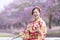 Japanese woman in traditional kimono dress holding sweet hanami dango dessert while walking in the park at cherry blossom tree