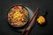 Japchae in black bowl on dark slate table top. Korean cuisine glass chapchae noodles dish with vegetables and meat