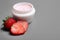 Jar of body cream and strawberries on grey . Space for text