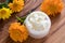A jar of calendula cream, with calendula flowers in the background