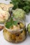 Jar of delicious artichokes pickled in olive oil and fresh vegetables on white table, closeup