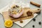 Jar with muesli, berries and yoghurt set on a cutting board surrounded by orange slice, cloves, berries and cinnamon stick