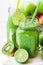 Jar mug with green vegetable smoothie, bottle with fruit juice, scattered kiwi, limes, apples