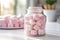 A jar of pink and white marshmallows basks in diffused light on a windowsill