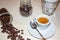 Jar with spilled coffee beans on linen tablecloth with cup of espresso full with spoon.