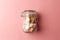 Jar with white sugar cubes and brown cane sugar lump on pastel pink background