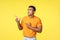 Jealous and upset gloomy cute masculine man, wear orange t-shirt, standing unhappy and sad over yellow background