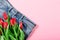 Jeans and bouquet of red tulips on pink background with copy space, empty text place. Advertising banner of fashionable casual