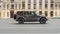 Jeep Wrangler Unlimited Sahara is driving in the cityscape. Side view of gray SUV in motion