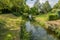 Jeker river with crystal clear water among green grass, trees, green vegetation and back gardens of houses