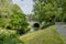 Jeker river between green grass, trees and abundant vegetation, a vehicular bridge and traffic lights in the background