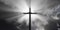 Jesus Christ christian crucifix or cross in front of stormy sky with dark clouds and sun rays or streaks, god, resurrection or