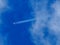 A jet flies across a blue cloudy sky leaving vapour trails