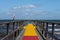 A jetty with a colourful carpet in blue, yellow and red. A blue ocean and sky in the background