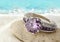 Jewelery ring with violet gemstone on sand beach with copy space