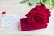 Jewelry gift box and bautiful red rose on wooden background. Whishing good morning on white piece of paper