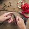 Jewelry making. Making bracelet of colorful beads. Female hands with a tool on a rough wooden table.