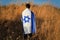 Jewish Israeli young man stands in a field with a large flag of Israel on his shoulders and back. Patriotic holiday concept