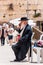 Jewish orthodox in black suit and hat sitting and drinking near the entrance alley to the Western Wall. People, locals and