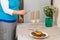 A Jewish woman in the dining room lights candles in Hanukkah on the table next to donuts and a vase of flowers.