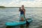 A Jewish woman in a headscarf in a pareo on her knees on a SUP board swims in the lake on a sunny day