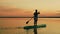 A Jewish woman swims on a sappboard in the evening in the golden reflections from the sunset on the sky and water