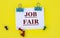 JOB FAIR - Word on white paper with clips on yellow background with buttons and pencil