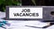 JOB VACANCIES is written on a gray file folder next to documents. Business concept