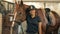 Jockey lady is standing near a brown horse and smiling