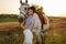 Jockey young girl petting and hugging white horse in evening sunset