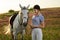 Jockey young girl petting and hugging white horse in evening sunset