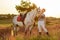 Jockey young girl petting and hugging white horse in evening sunset. Sun flare