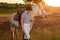 Jockey young girl petting and hugging white horse in evening sunset. Sun flare