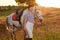 Jockey young girl petting and hugging white horse in evening sunset. Sun flare